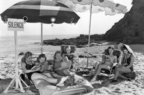A black and white image of a book club meeting on a beach and reading silently together.
