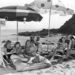 A black and white image of a book club meeting on a beach and reading silently together.