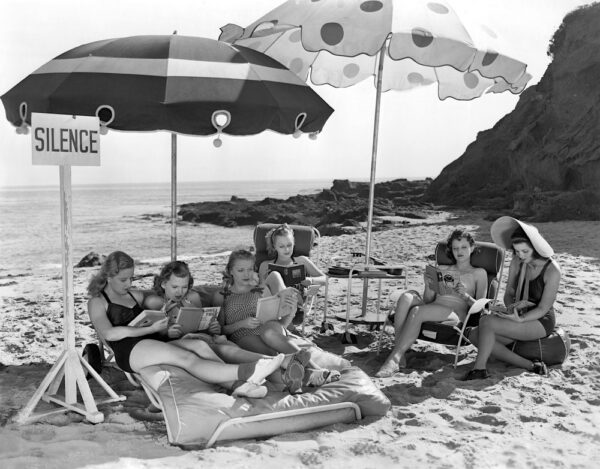 A black and white image of a book club meeting on a beach and reading silently together.